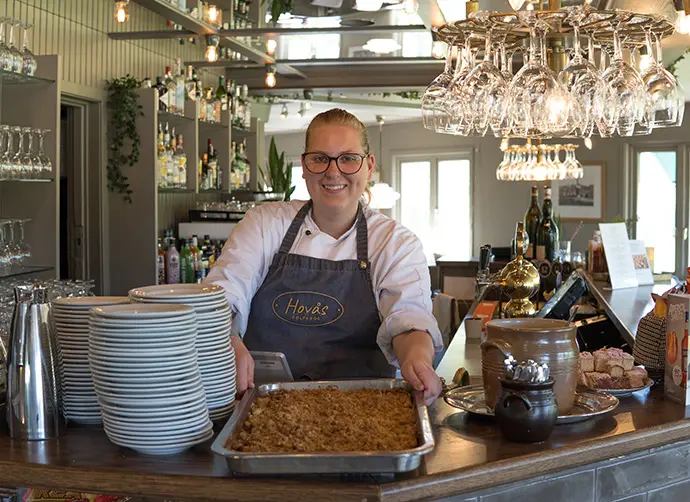Elev på APL i restaurangmiljö presenterar maträtt bakom disk.