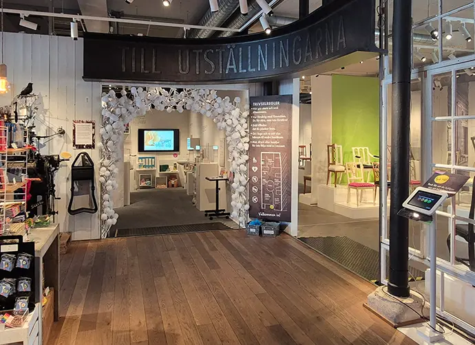 Entrén till två av museets utställningar från butiken. Över ingångarna sitter en stor skylt med texten till utställningarna.