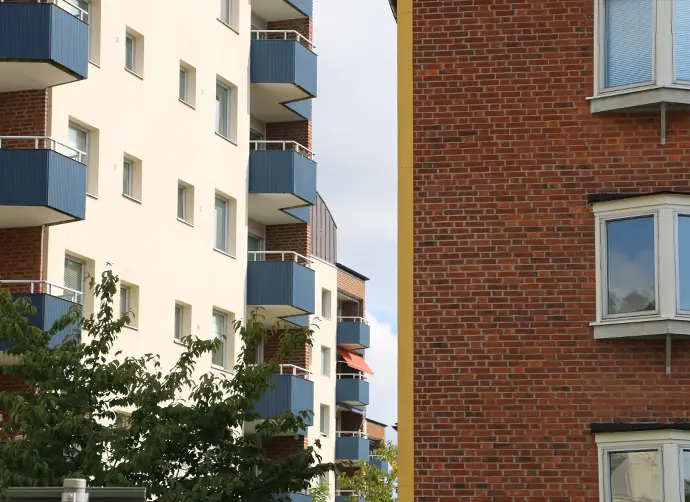 Två olika husfasader, en i ljus puts med tegeldetaljer och blå balkonger och en med rött tegel.