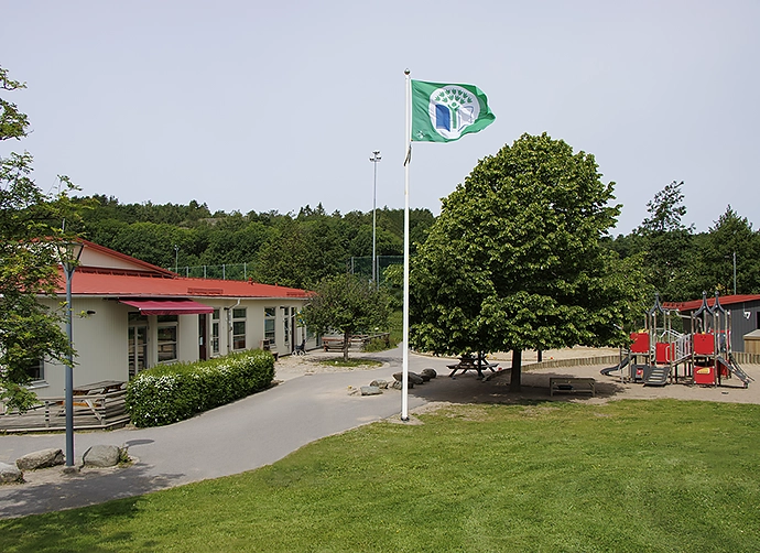 Förskolegård med gräsmatta och flaggstång framför förskolan