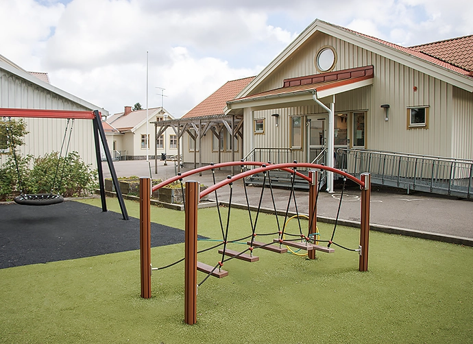 Skolbyggnad med gunga och klätterställning i förgrunden