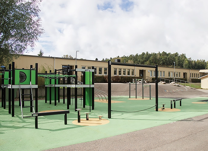 skolbyggnad med skolgård och grön klätterställningi förgrunden