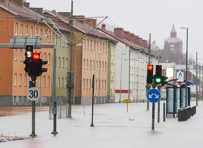 En gata med trafikljus i stadsmiljö är översvämmad av vatten. En spårvagnshållplats är också översvämmad. 