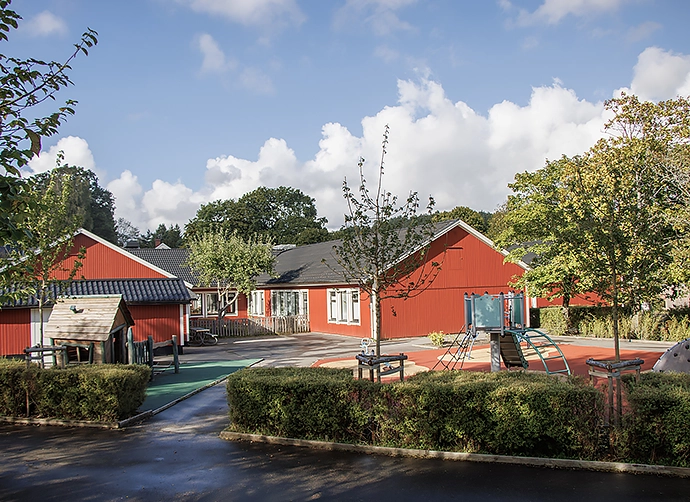 grönskande träd och buskar på gården med den röda förskolan i bakgrunden