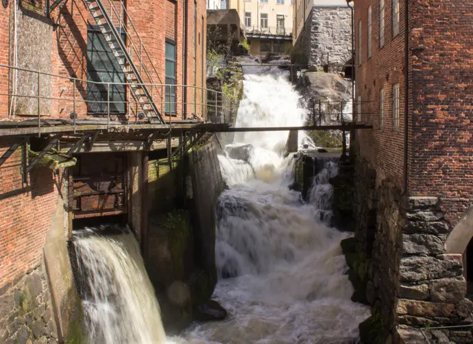 Forsen som dånar ner mellan tegelbyggnader i den gamla industrimiljön Kvarnbyn.