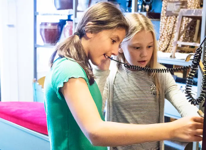 Två barn i 10-årsåldern lyssnar och tittar på en aktivitet i en utställning.