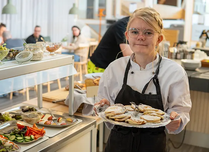 Elev presenterar fat med bakverk i restaurangmiljö.