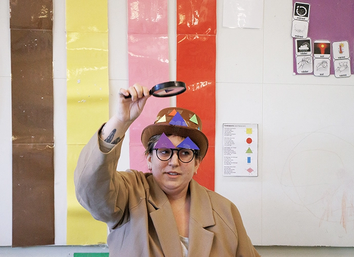 utklädd pedagog på förskolan med hatt med former på. Klädd i rock och förstoringsglass