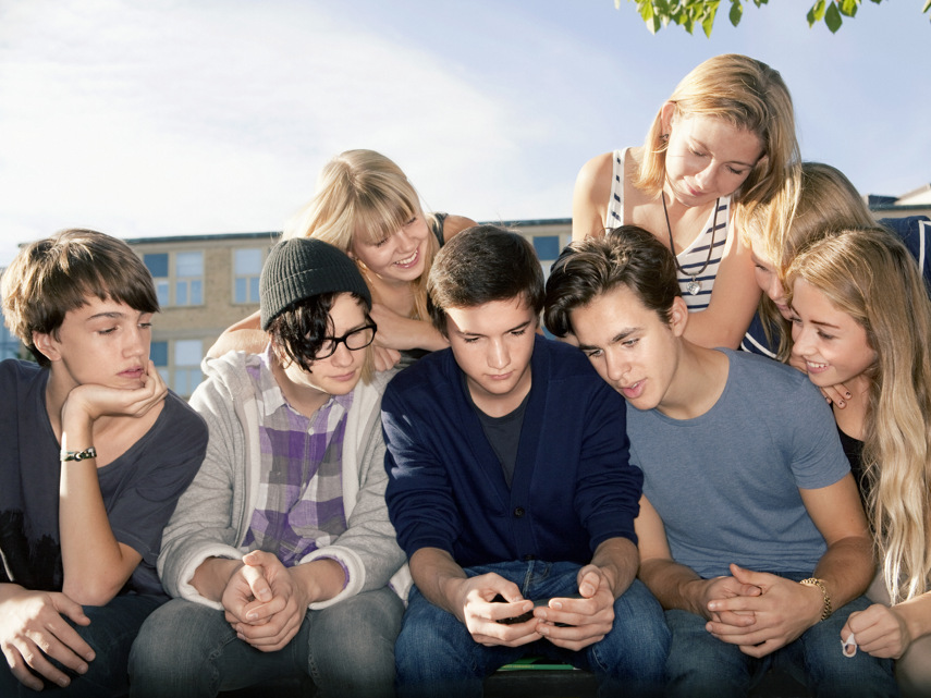 En grupp med ungdomar sitter och tittar på en mobiltelefon