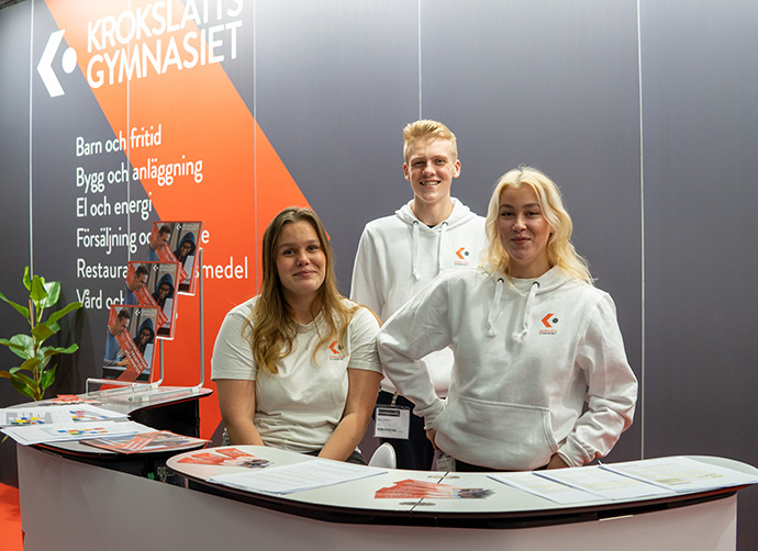 Elever står vid monter och möter besökare på gymnasiemässan.