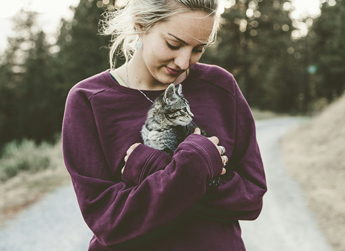 Person håller katt utomhus i naturmiljö.