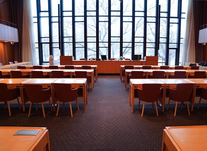 Mölndals fullmäktigesal, ett stort rum med flera rader av bord och stolar framför ett stort väggtäckande fönsterparti .