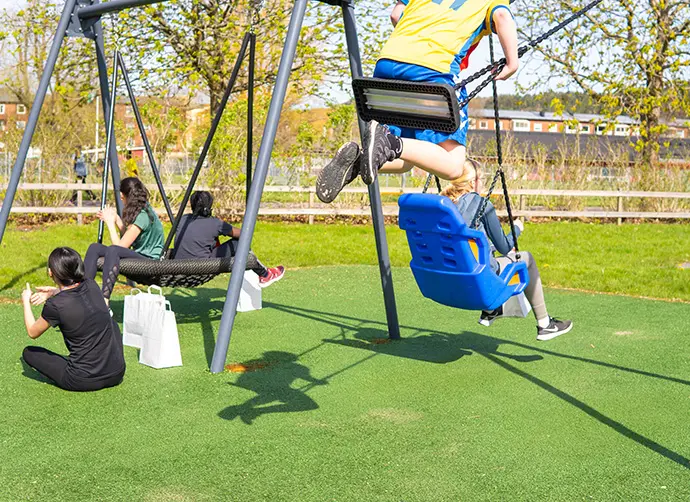 Elever leker och gungar på en skolgård en solig dag.