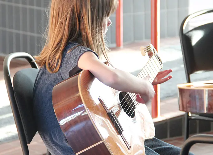 Ett barn sitter på en stol och spelar på en akustisk gitarr