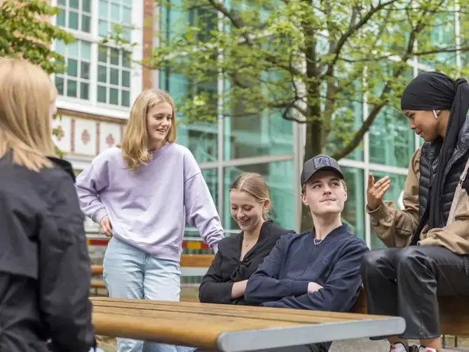 Elever utanför skolan sittandes och stående runt ett bord.