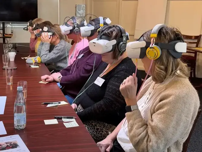 Personer sitter runt ett bord med VR-glasögon och hörlurar.