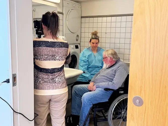 En man i rullstol och en kvinnlig vårdgivare filmas på ett vård- och omsorgsboende.