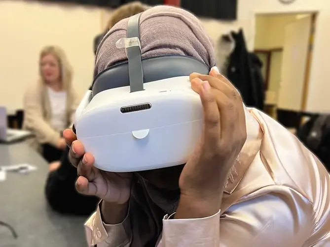 En kvinna med VR-glasögon sitter med ansiktet vänt mot kameran.