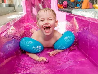 Skrattande pojke i vattenrutschbanan i Lilla lekbassängen i Åbybadet.