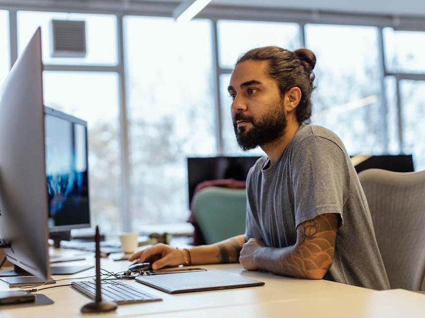 En man sitter framför en datorskärm på sin arbetsplats.