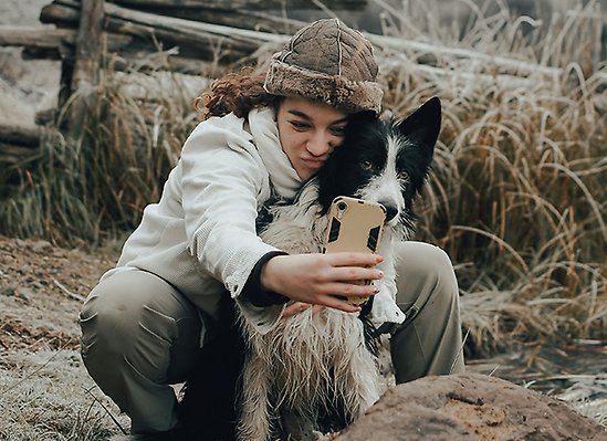 Person tar selfie med hund utomhus i natur.