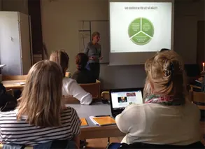 pedagoger sitter i ett mörkt rum och tittar på en presentation på storbild