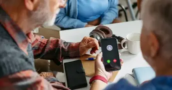 En person pekar på en smartphone som ringer. En mugg och hörlurar syns på bordet.