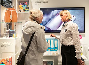 Två kvinnor i samtal i en utställningsmiljö fylld med hygienartiklar.