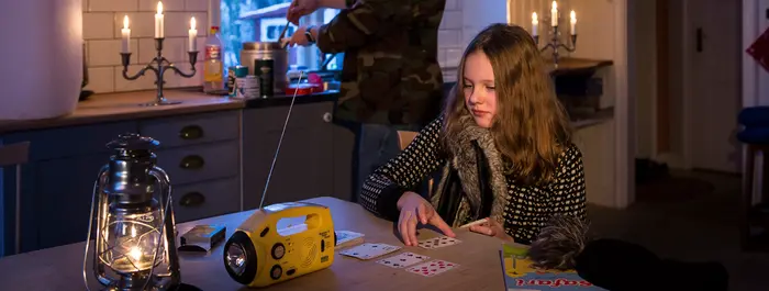 I ett nedsläckt rum sitter en flicka och spelar kort. På bordet finns en radio och en ljuslykta.