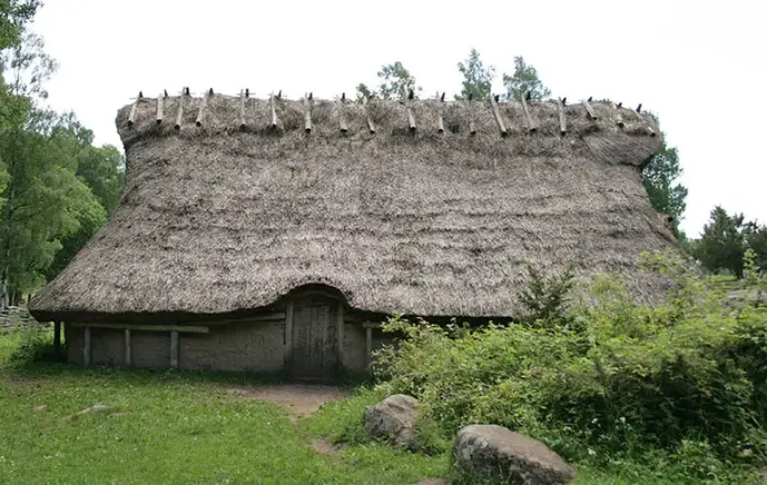 Ett hus som ska likna ett hus från bronsåldern. Huset har ett vasstak och byggt i trä. 